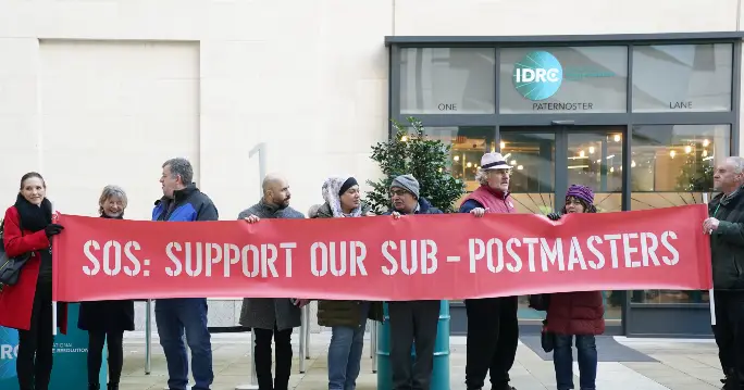 A group of people holding signs and banners protesting outside a Post Office or a courthouse, highlighting the public outcry and the fight for justice.