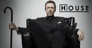 House MD Hugh Laurie Title character sitting on a black armchair holding his black cane