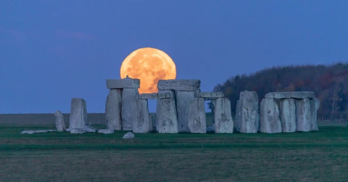 A full moon rises majestically over Stonehenge, illuminating the ancient stones during the solstice in England.