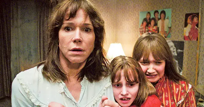 In a shadowy room, a woman and two girls appear, capturing a moment filled with suspense inspired by The Conjuring 2.