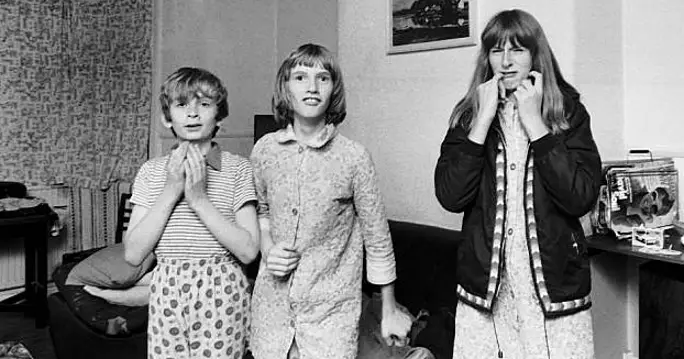 one boy and 2 girls wear 1970 pyjamas gathered in a living room, an atmosphere of suspense surrounding them, linked to the Enfield Poltergeist phenomena. 