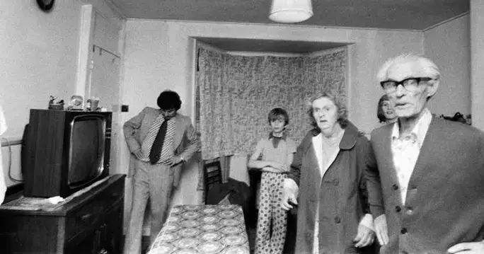 A black and white photo featuring individuals in a living room, reflecting the mysterious aura of the Enfield Poltergeist phenomena.